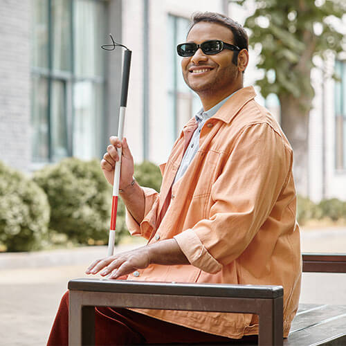 Homem com deficiência visual sentado no banco de uma praça
