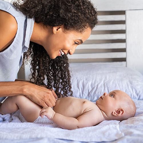 Mulher preta rindo e brincando com filho em cima da cama